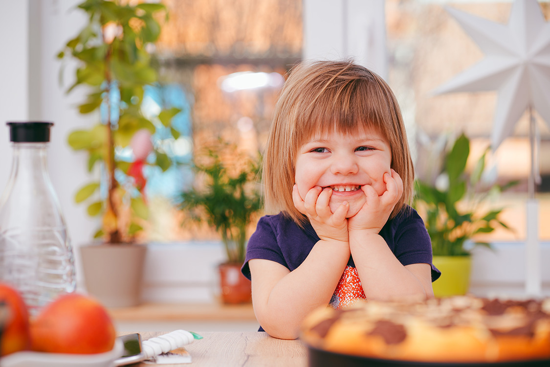 Kleines Mädchen sitzt am Frühstückstisch und lächelt
