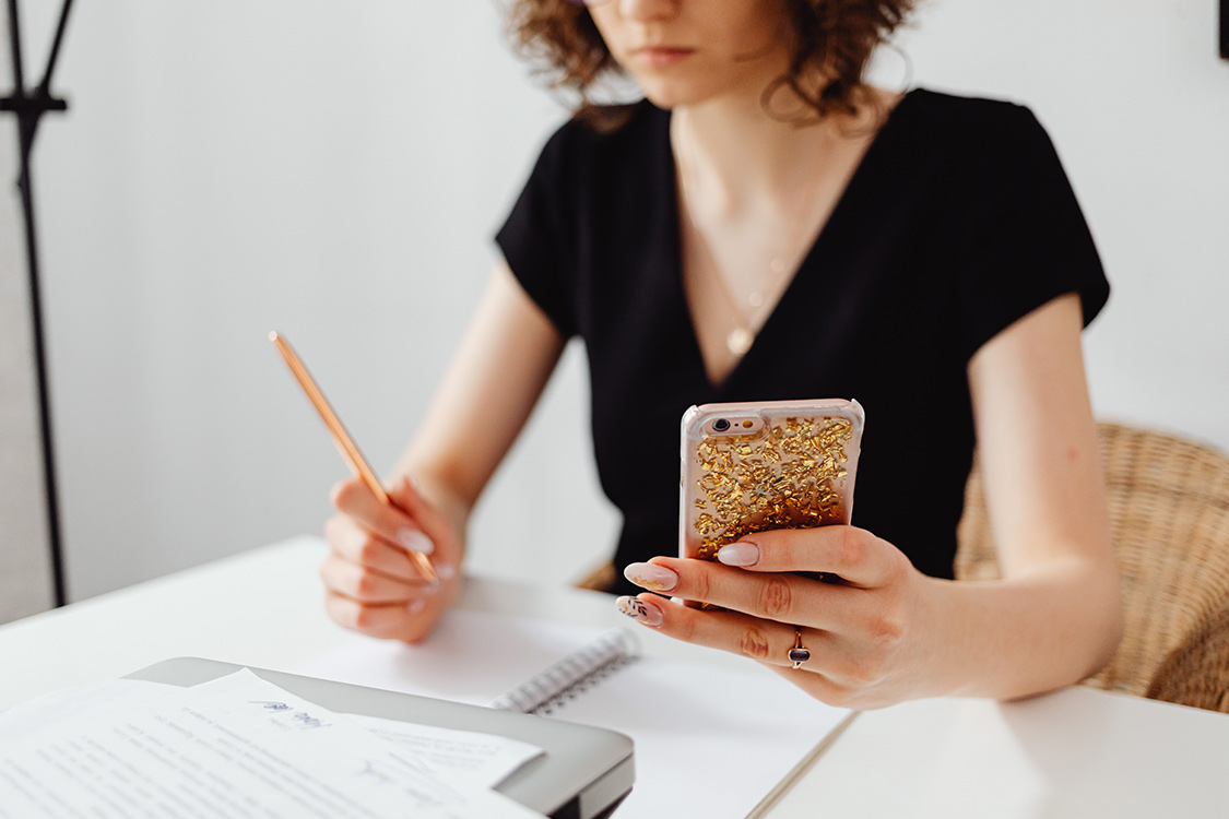 Frau schreibt sich Informationen vom Handy auf