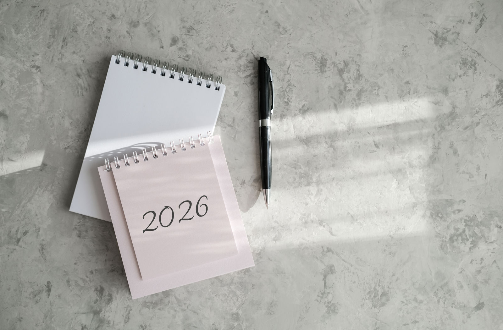 Kalender mit der Jahreszahl 2026 und schwarzer Stift auf einer hellgrauen Tischfläche